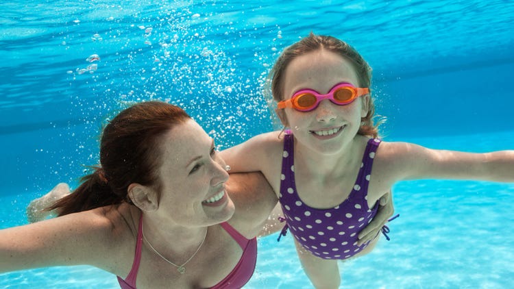 A mother and daughter smile as they swim under water.