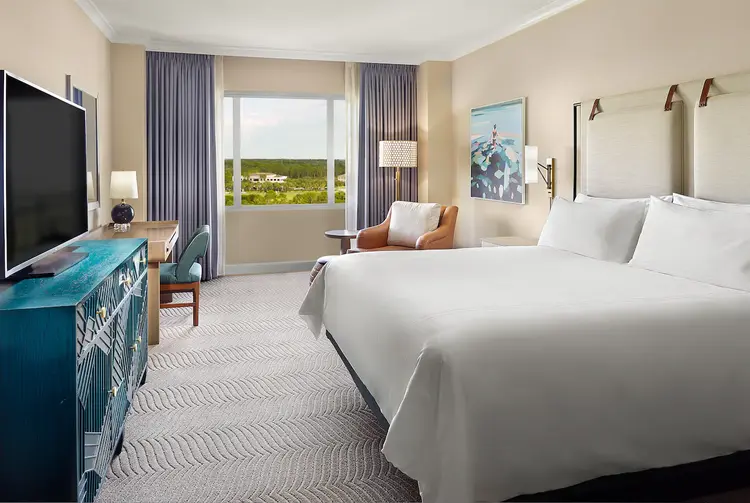 A hotel room featuring a king size bed, dresser, television, armchair and desk space
