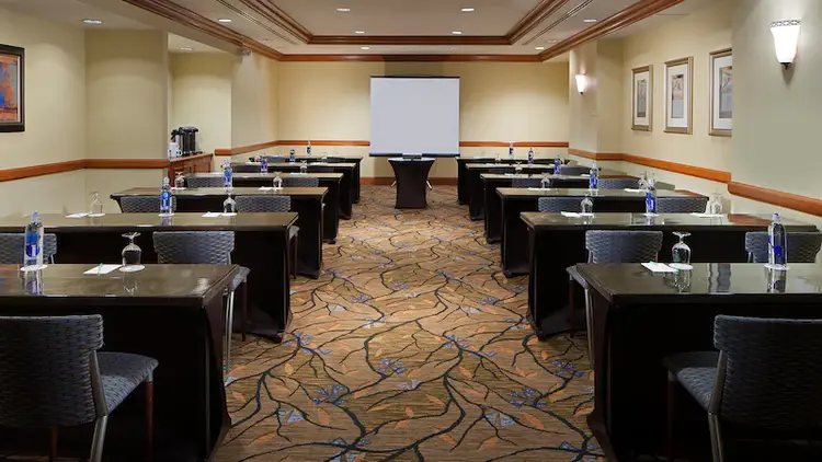A meeting room with a projector screen, a lectern, 12 meeting tables and 24 chairs
