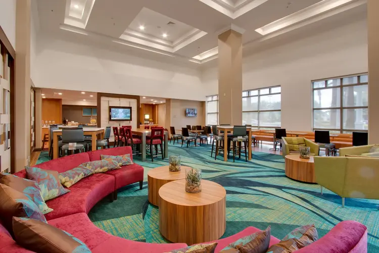 High-ceilinged dining area with tables and chairs, armchairs, a large curved sofa and kitchenette