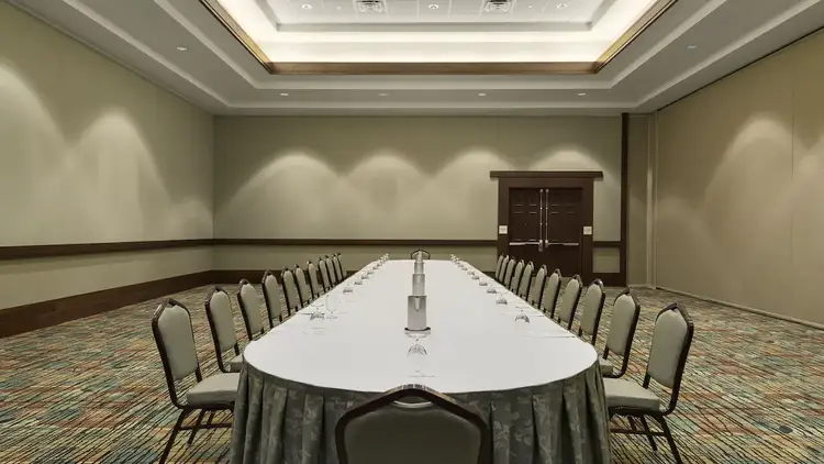 A convention room with a long oval table, 24 chairs and pitchers of water with glasses.