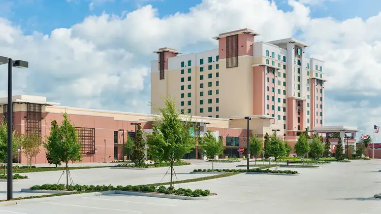 The front parking lot of Embassy Suites Lake Buena Vista South, with young trees near the main entrance.