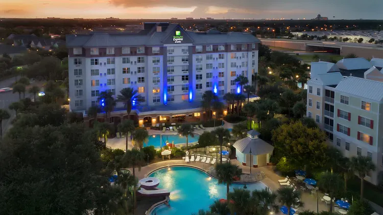 The outside of the hotel at nighttime featuring palm trees and a pool area