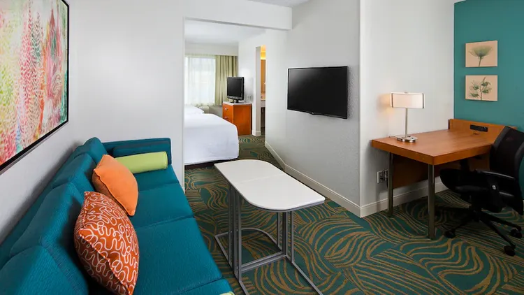 A sofa with 2 tray stands across from a wall mounted TV and a desk with a rolling chair
