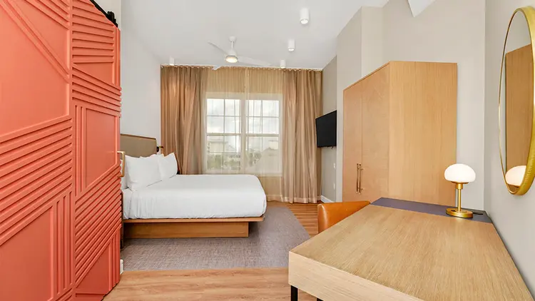 A room at Embassy Suites by Hilton Orlando Sunset Walk with a king size bed, a desk, a lamp, a dresser, a TV and a window with outside views