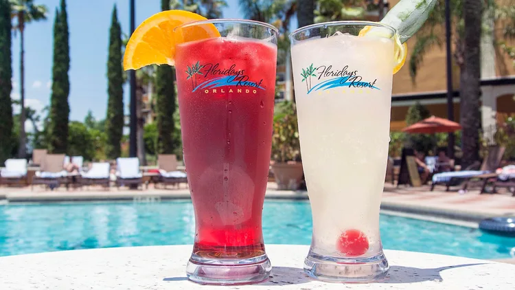 Two cold drinks in glasses on a table by a swimming pool