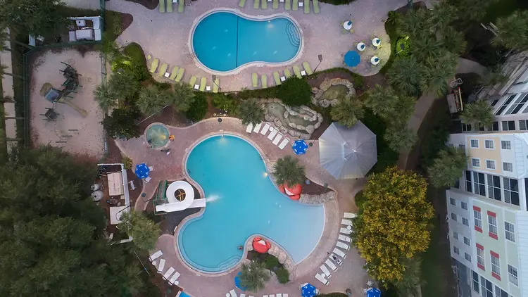 2 swimming pools surrounded with lounge chairs including one pool featuring a water slide