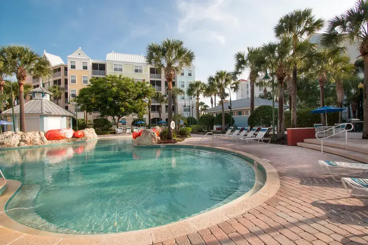 Curved step-in area of outdoor pool area with chaise lounges and palm trees, next to hotel