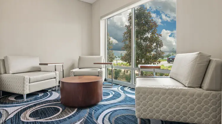 Two sofas and an armchair with tables near a plate glass window that reveals a tree and clouds outside