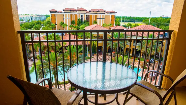 Two chairs and a table on a hotel room balcony with the pool area and hotel towers in the background