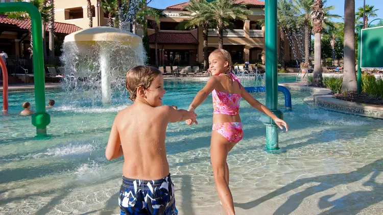 A girl takes her brother’s hand and leads him into a water play area