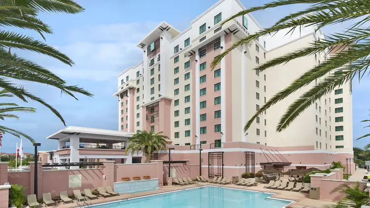Behind the hotel, chaise lounges surround a large pool with privacy walls and umbrella tables.