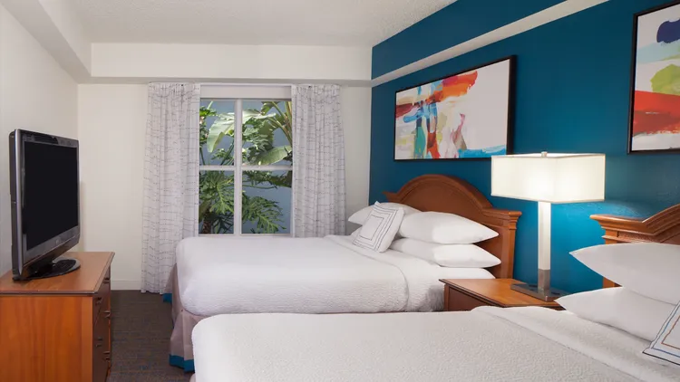 A hotel room featuring 2 queen size beds, dresser and television