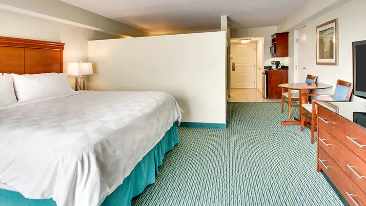 A hotel room featuring a king size bed, dresser, sitting table and kitchenette