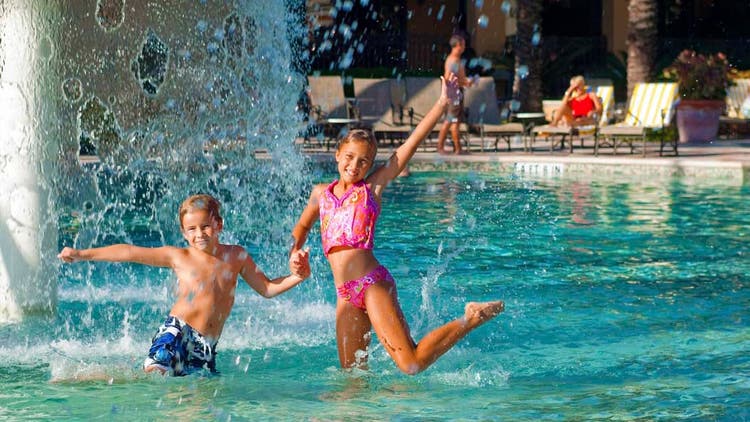 A boy and girl in a fun pose beneath a fountain in a kids’ water play area