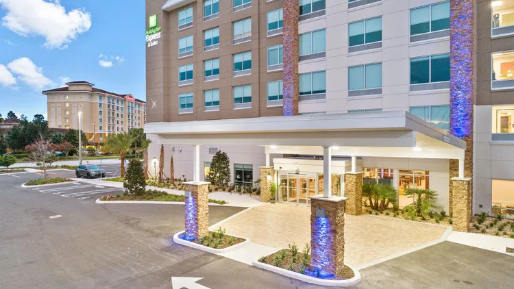 The entry to a hotel with a concrete awning and a sign that reads, ‘Holiday Inn Express and Suites’