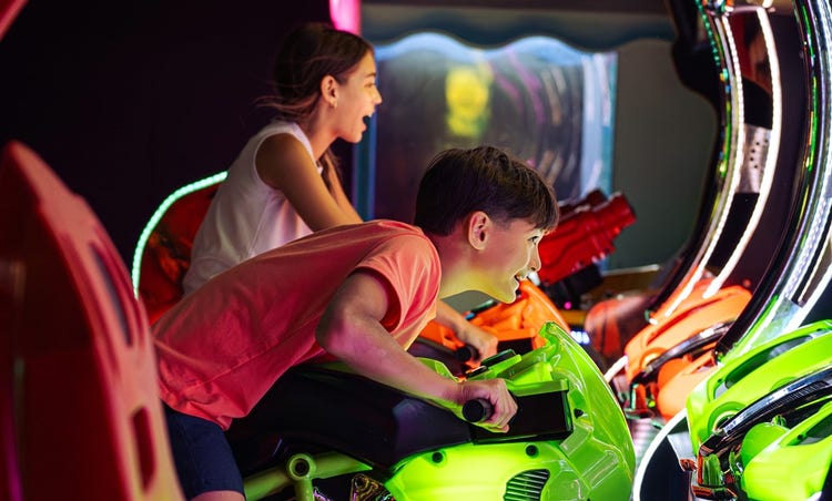 A boy and girl laughing while riding a motorcycle simulator arcade game