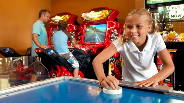 A girl playing air hockey in an arcade with video games and a claw machine